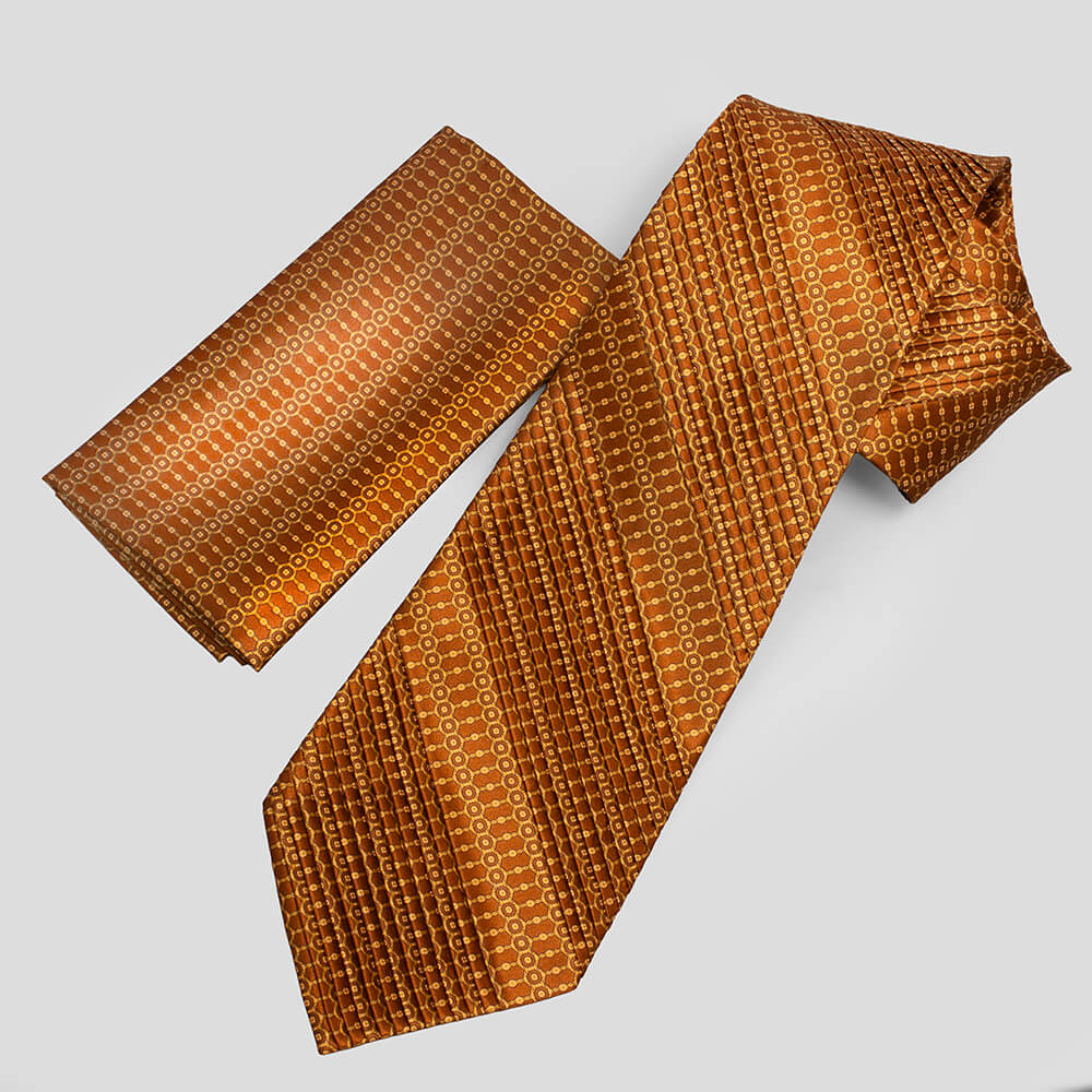 オレンジのプリーツネクタイと共布のポケットチーフセット。幾何学模様が美しく整列している。A pleated silk necktie and matching pocket square in vibrant orange, featuring symmetrical geometric patterns.